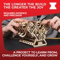 Gedetailleerd houten V8-motor model, waarbij de mechanica zichtbaar is. Twee handen houden het vast. Tekst: THE LONGER THE BUILD THE GREATER THE JOY.