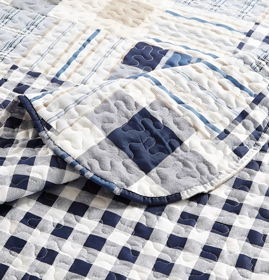 Detail van een dekbedovertrek met vierkantjes en ruitjes in blauw, wit en grijs. Gingham ruit aan de rand.