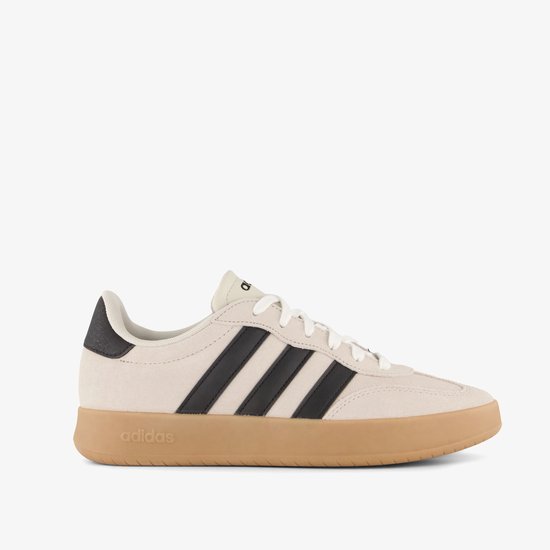 Zijkant van beige Adidas sneaker met zwarte strepen, witte veters en gummen zool.