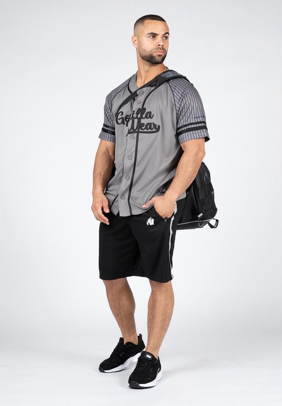 Man met grijze baseball jersey, zwarte shorts, sneakers en een zwarte tas over zijn schouder.
