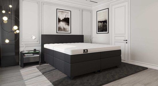Zwarte boxspring met matras in een moderne slaapkamer. Liggend op een donkergrijs vloerkleed.