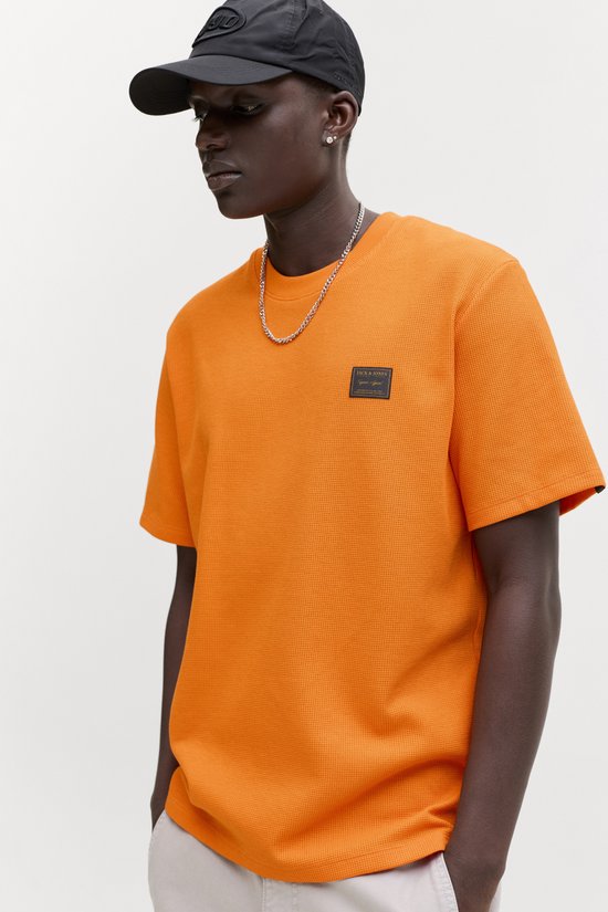Model draagt een oranje wafel t-shirt met Jack & Jones logo, zilveren ketting en zwarte pet.