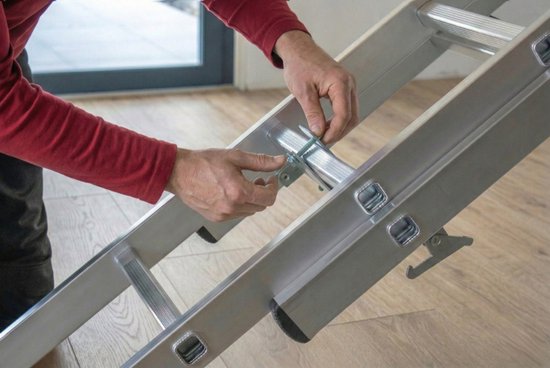 Man met rode trui bevestigt metalen trapadapter aan aluminium ladder.