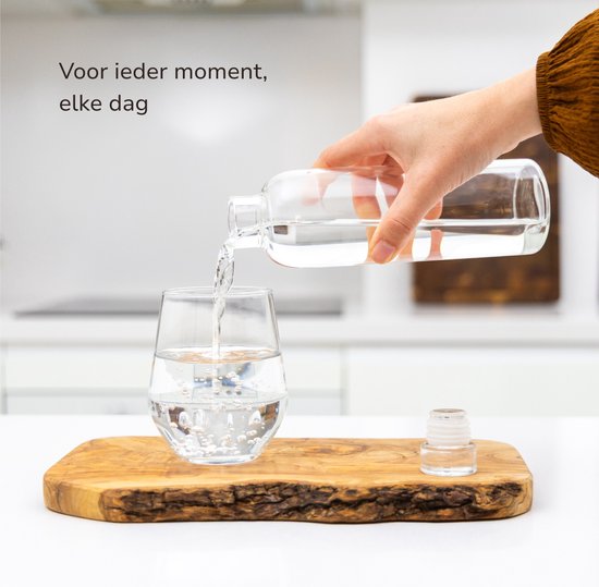 Hand schenkt water uit glazen fles in glas.