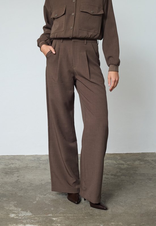 Model draagt een bruine wijde broek met hoge taille, met steekzakken.
