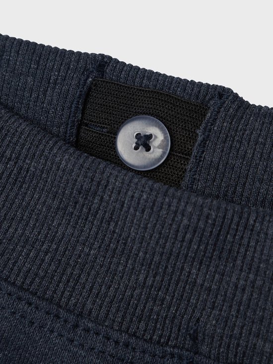 Detail van de tailleband van een donkerblauwe joggingbroek met een knoop.