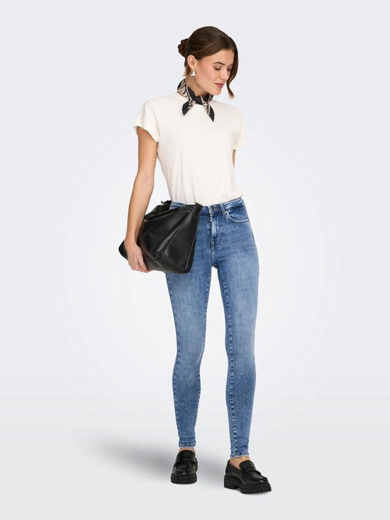 Model in een witte top, sjaaltje met panterprint en een lichtblauwe skinny jeans met stonewash-effect. Houdt een zwarte tas vast.