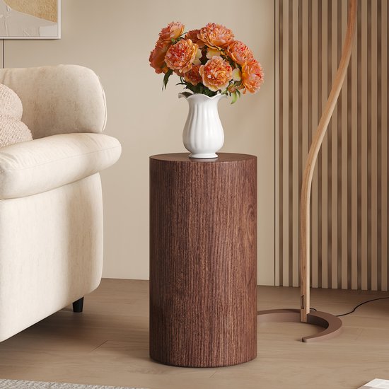 Walnoothouten bijzettafel naast een beige bank en een vloerlamp, met een vaas met oranje bloemen.