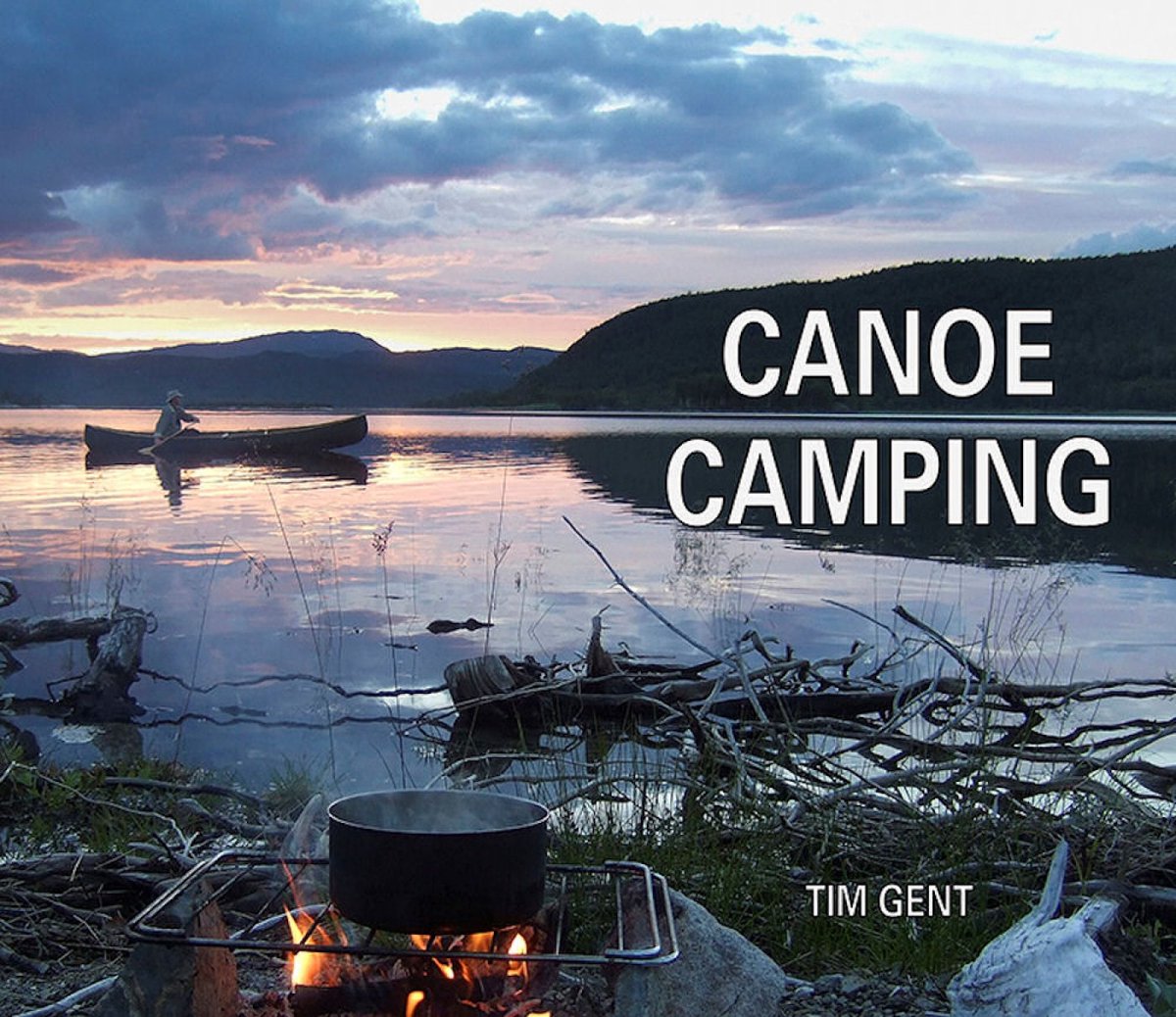 Een kampvuur kookt in de voorgrond, met een kano op een meer in de achtergrond tijdens de schemering. Tekst 'CANOE CAMPING' staat op de voorgrond.