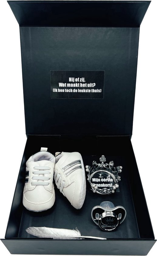 Zwarte geschenkdoos met witte babyschoentjes met zilveren strepen, een kroon en een speen. Tekst op de kroon: 'Mijn eerste sneakers!'.
