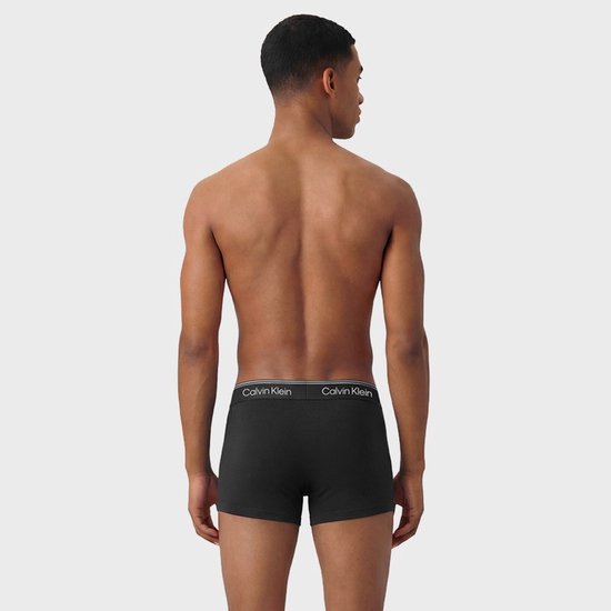 Man met zwarte Calvin Klein trunks, staand van achteren gezien.