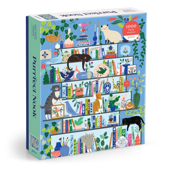 Doos van een 1000-delige puzzel met de titel "Purrfect Nook", met een blauwe achtergrond met boekenplanken vol katten, planten en decoraties.