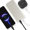 Lichtgrijze powerbank met "10" laadt een smartphone op, naast zwarte oortjes.