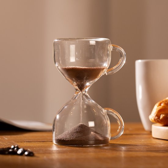 Sablier en verre avec poignées et sable brun, sur une table en bois.