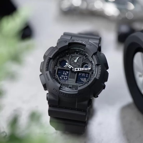 Zwarte G-Shock horloge met analoge en digitale wijzerplaat, op een glanzend oppervlak.