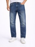 Man in een wit T-shirt en een stonewashed blauwe jeans. De jeans heeft extra naden op de bovenbenen en witte sneakers.