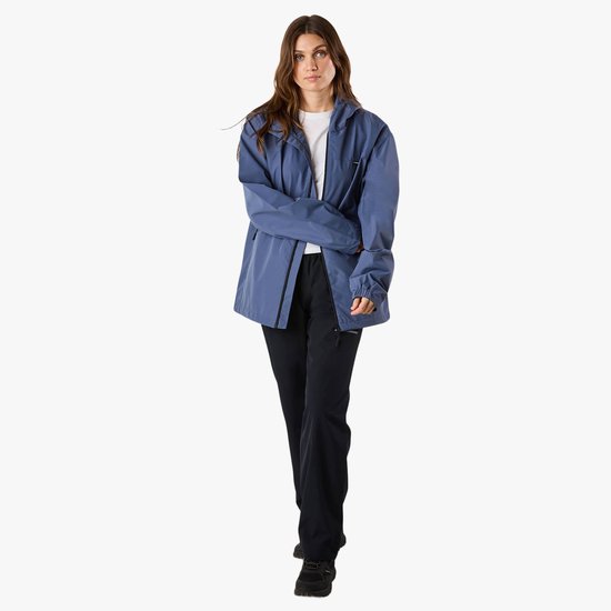 Vrouw in een blauw X-Trail windjack met capuchon en zwarte broek, handen gekruist voor zich.