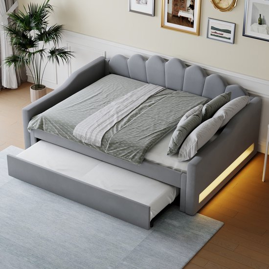 Lit de jour gris aspect lin avec lit gigogne, coussins, éclairage LED jaune et plante en arrière-plan.