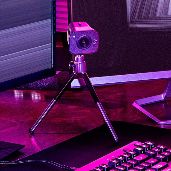 Webcam Logitech StreamCam sur un trépied, à côté d'un clavier et d'une souris, avec un éclairage violet.
