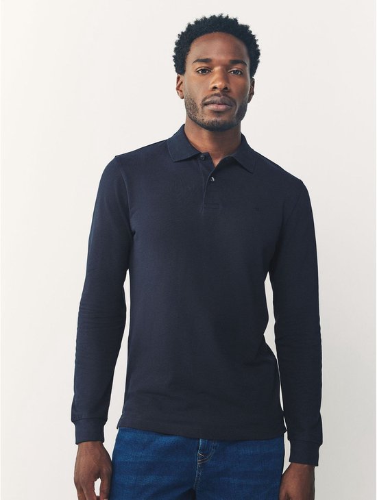 Man in een donkerblauwe polo met lange mouwen en jeans, staand van voren gezien.