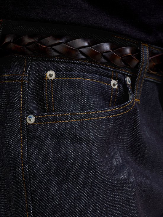 Close-up van de zak van een donkerblauwe jeans met gele stiksels en een gevlochten bruine riem.