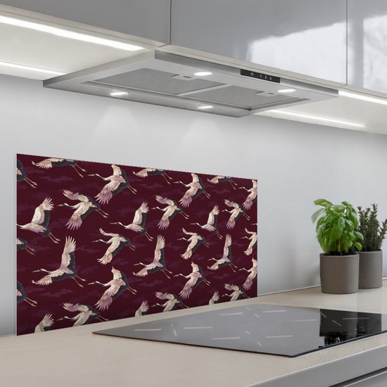 Glanzend spatscherm met patroon van kraanvogels op bordeauxrode achtergrond, boven een modern fornuis.
