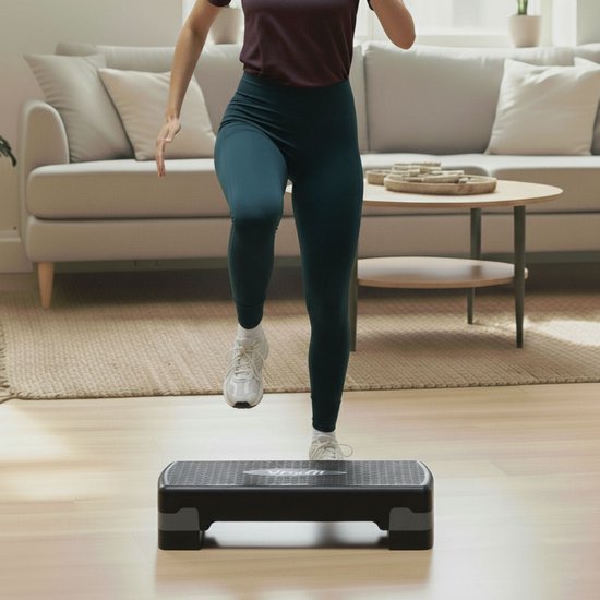 Vrouw traint met een zwarte aerobic step in een woonkamer.