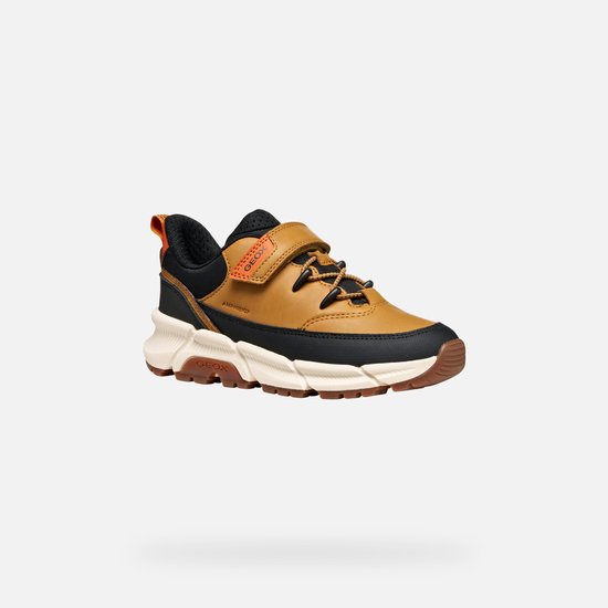 Bruine sneaker met zwarte en oranje accenten, oranje lus en klittenbandsluiting.