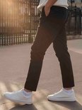 Een persoon draagt een donkerbruine broek en witte sneakers met witte enkelsokken.
