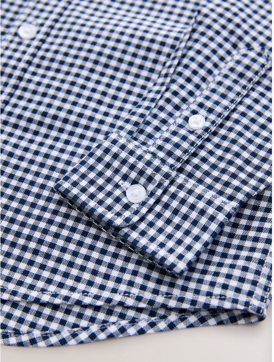 Detailopname van de manchetten van een blauw met wit vichy ruitpatroon overhemd.