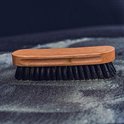 Brosse à manche en bois et poils noirs, posée sur une surface sombre avec du sable.