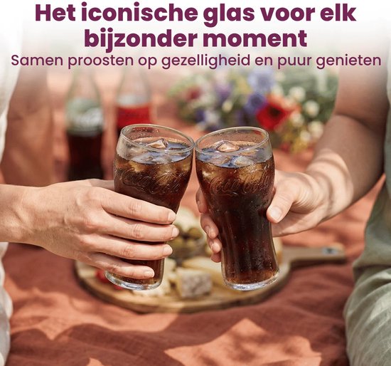 Deux mains lèvent un verre Coca-Cola avec du cola et des glaçons pour trinquer, avec une couverture de pique-nique et de la nourriture en arrière-plan.