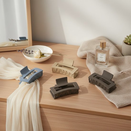 Vier grote matte haarclips in blauw, beige en grijs op een houten dressoir.