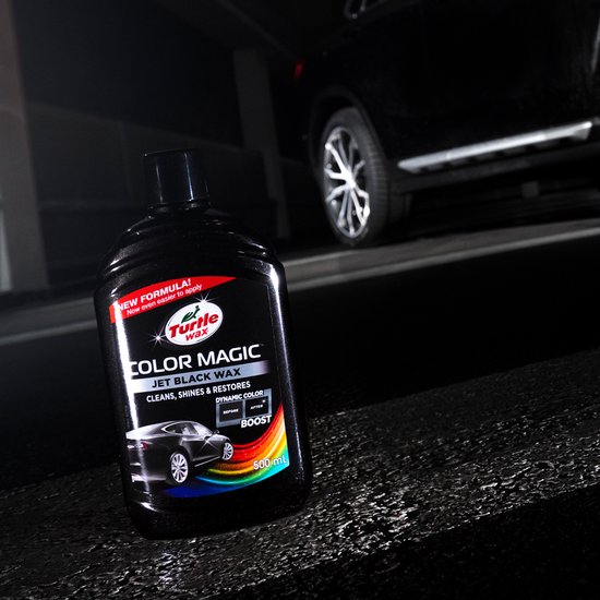 Fles Turtle Wax Color Magic Jet Black Wax op een donkere, nat uitziende ondergrond naast een glimmende zwarte auto.