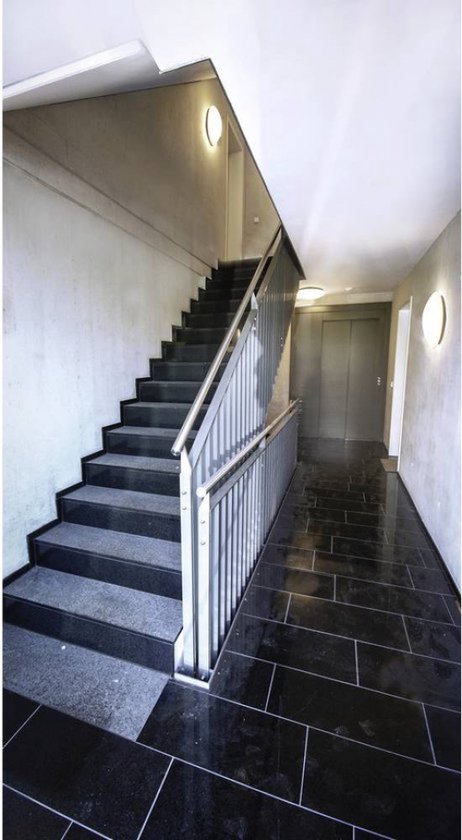 Moderne hal met marmeren vloer, trap met metalen leuning en een lift.