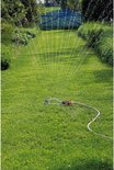 Zwenksproeier sproeit water op een grasveld met blauw hek in de verte.