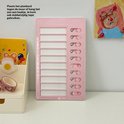 Roze planbord op een bureau, naast een organizer met stickers. Het planbord heeft een takenlijst met schuifjes.