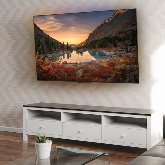 Un grand téléviseur à écran plat affichant un paysage, monté sur un mur au-dessus d'un meuble TV blanc.