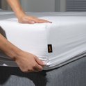 Vrouw handen die een wit hoeslaken over een matras trekken, merklabel zichtbaar.