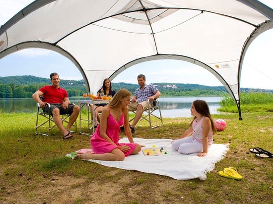 Mensen ontspannen onder een Coleman partytent aan de oever van een meer.