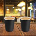 Twee zwarte papieren bekers met koffie, op een houten tafel.