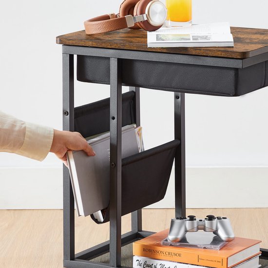 Detail van de onderkant van een bijzettafel met metalen frame en wieltjes. Een hand pakt een boek uit het zwarte opbergvak.