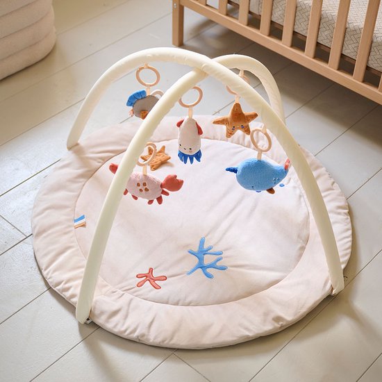 Beige ronde babygym met een speelkleed met zeedieren, en een speelboog met vijf zachte speeltjes.