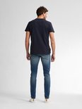 Man met kort bruin haar, staand van achteren gezien, draagt een marineblauw t-shirt en een vaalblauwe slim fit jeans.