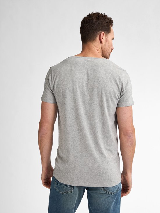Man draait zich om, draagt een grijs basic T-shirt met korte mouwen en blauwe jeans.