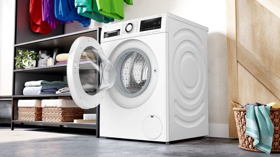 Witte Bosch wasmachine met open deur, gevuld met schone was, naast een mand met wasgoed.