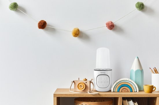 Witte Lionelo flesverwarmer met display, naast een houten camera en een regenboogdecoratie.