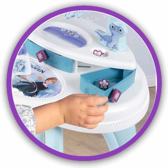 Een kinderhand trekt aan een blauw laatje van een wit kaptafeltje met Frozen-afbeeldingen, kammen en een blauw figuurtje.
