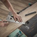 Een man gebruikt een wolfcraft winkelhaak en schaalverdeling om een houten vloer te markeren.