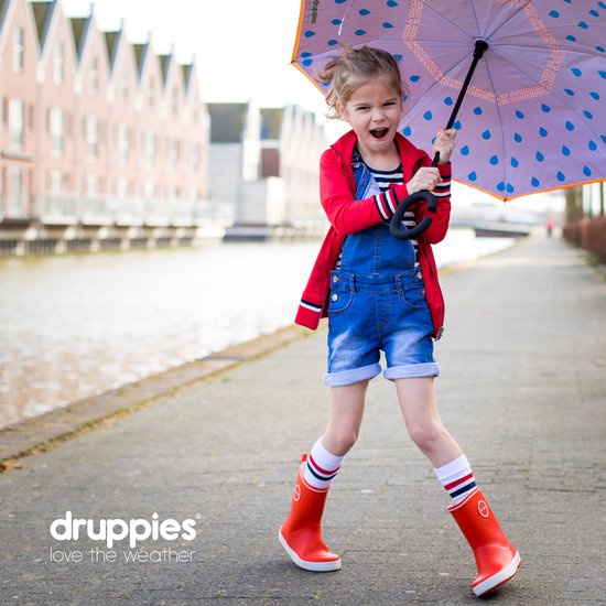 Een lachend meisje in een rode jas, blauwe tuinbroek en oranje laarzen met regenjas en paraplu.